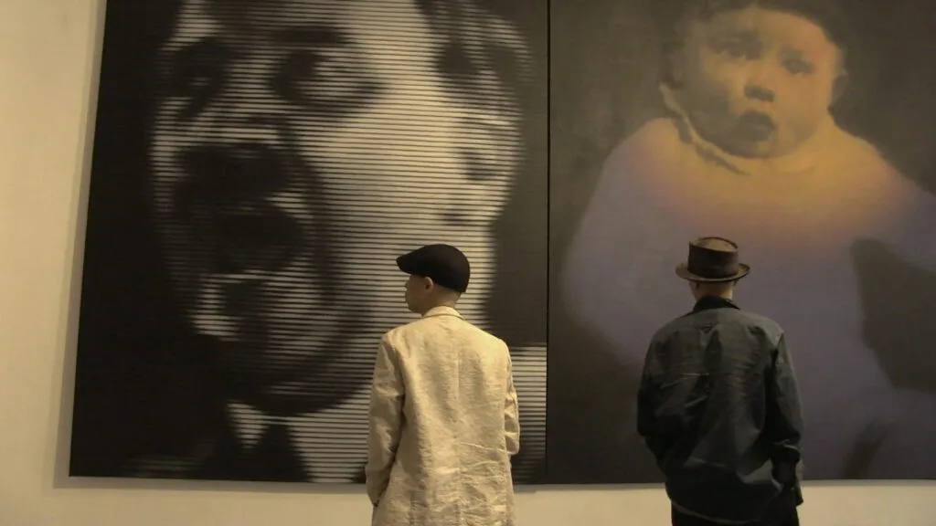Two artists look at their large-format images in an exhibition.