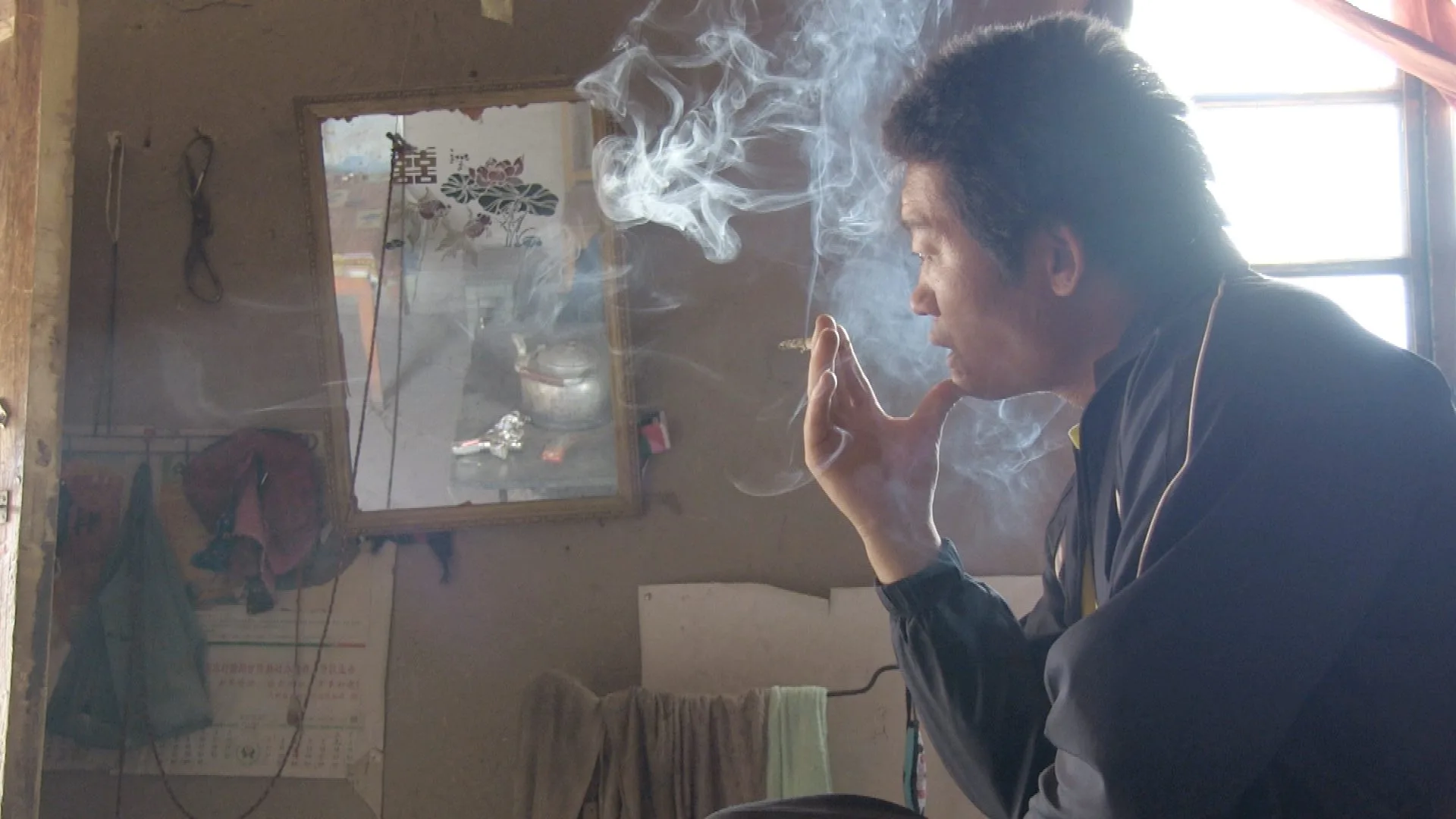 Vignette du film Watermarks (2013) : Un homme fume près d’une fenêtre dans une pièce simple, tandis que la fumée monte dans le contre-jour.