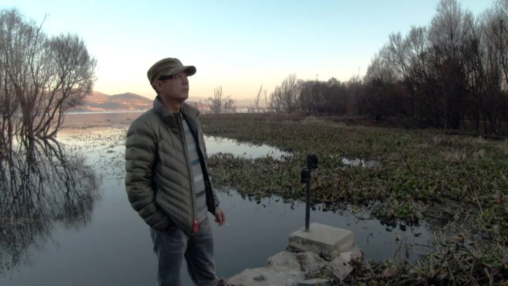 A man stands on a quiet shore in a wintry landscape.
