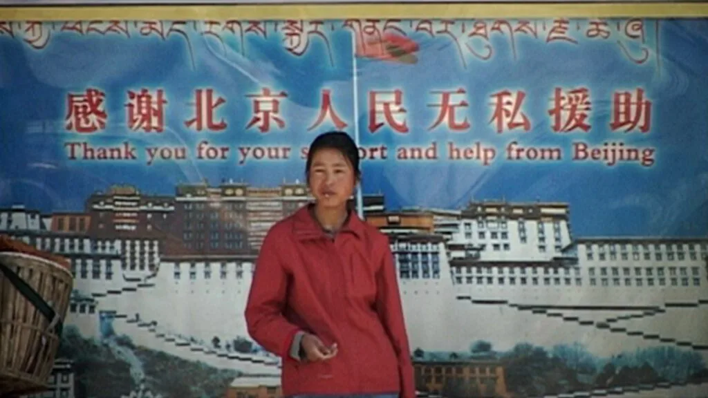 Une femme se tient devant une affiche de propagande montrant le palais du Potala et des caractères chinois.