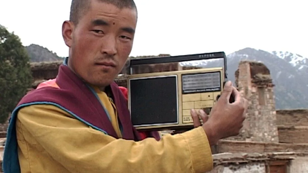 Un moine dans l’est du Tibet tend une radio vers la caméra.