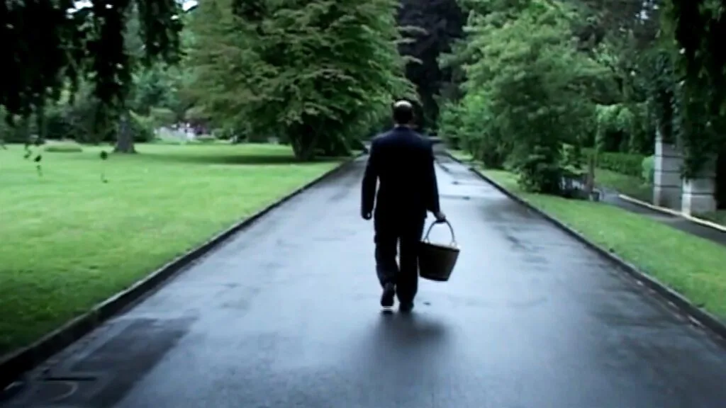 A man carrying an urn in a basket along a quiet cemetery path.