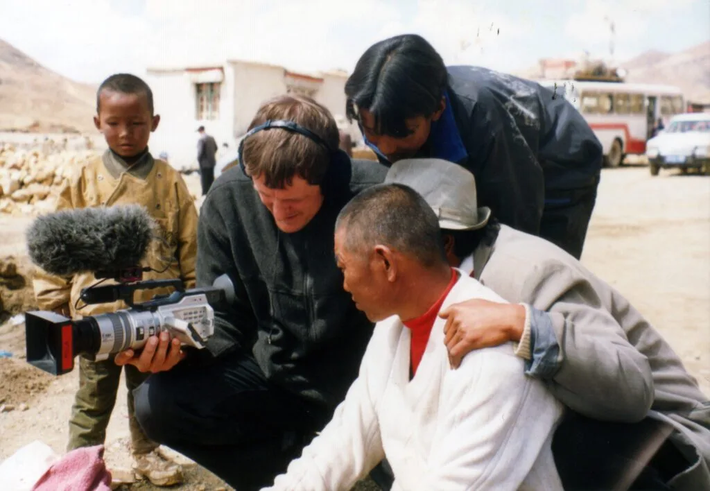 Luc Schaedler avec une caméra, entouré d’un groupe de Tibétains.