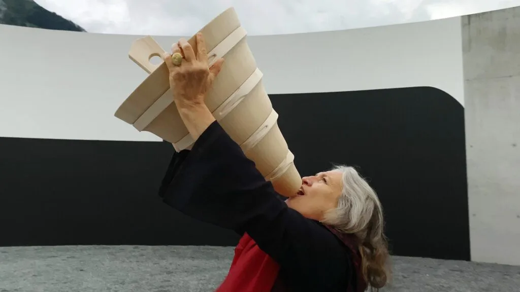 Vignette du film Loba Loba (2021) : Une femme soulève un entonnoir surdimensionné au-dessus de sa tête dans une sculpture contemporaine en béton.